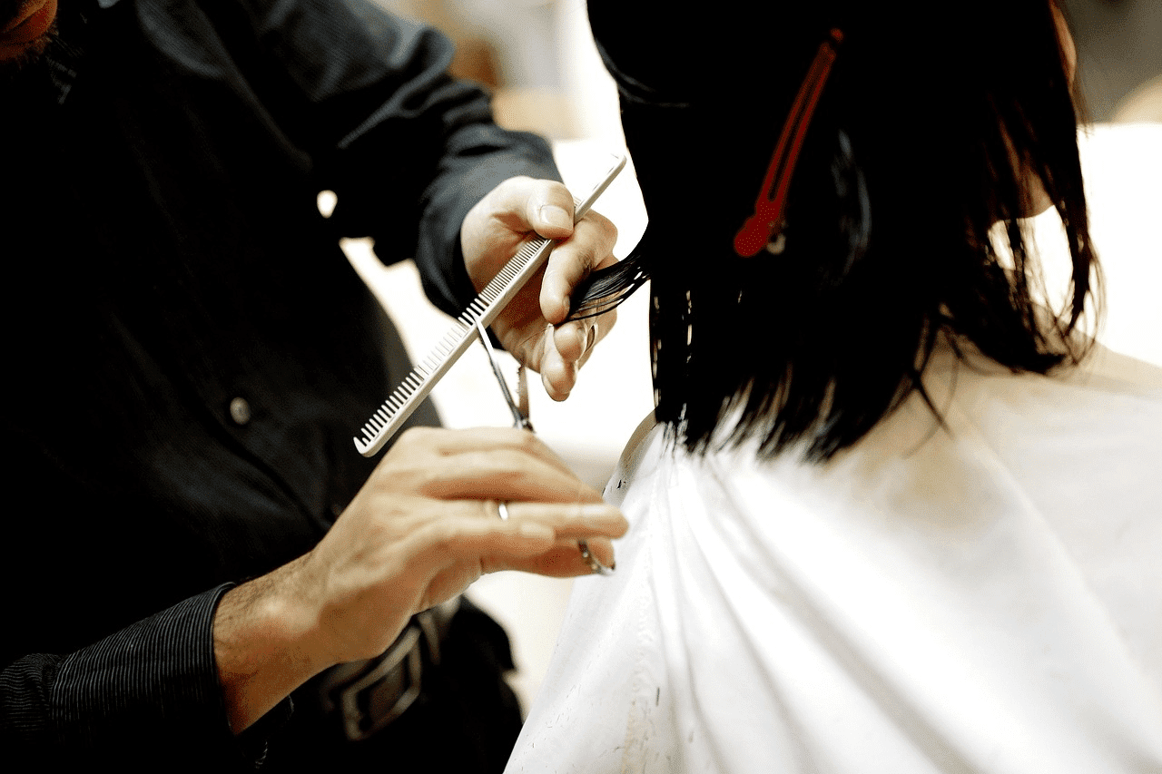 Hairdresser cutting a client's hair with scissors in a salon.