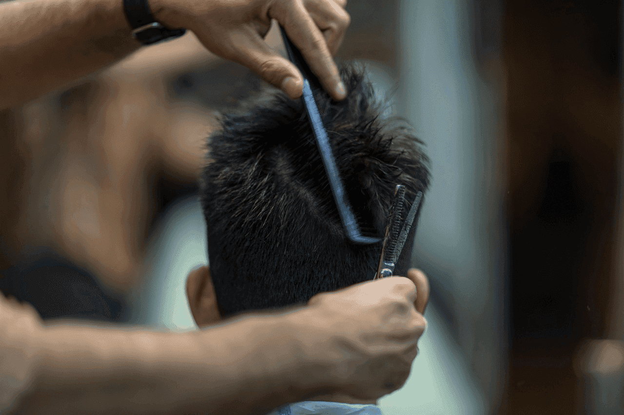 Person receiving a haircut, stylist using comb and scissors.