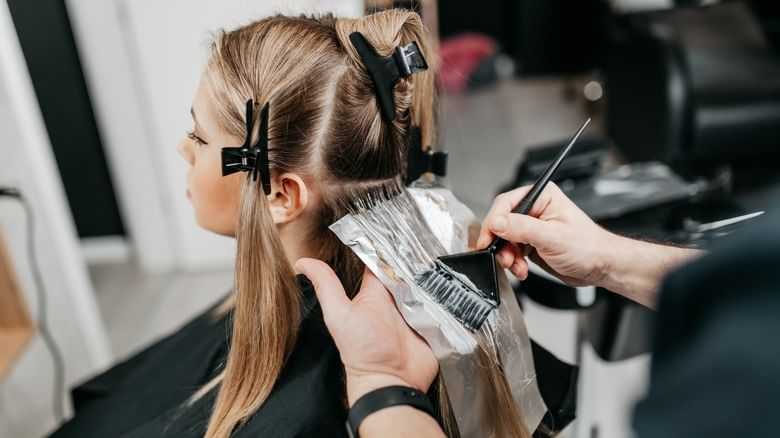 Hairdresser applying foil highlights to woman's hair in salon.