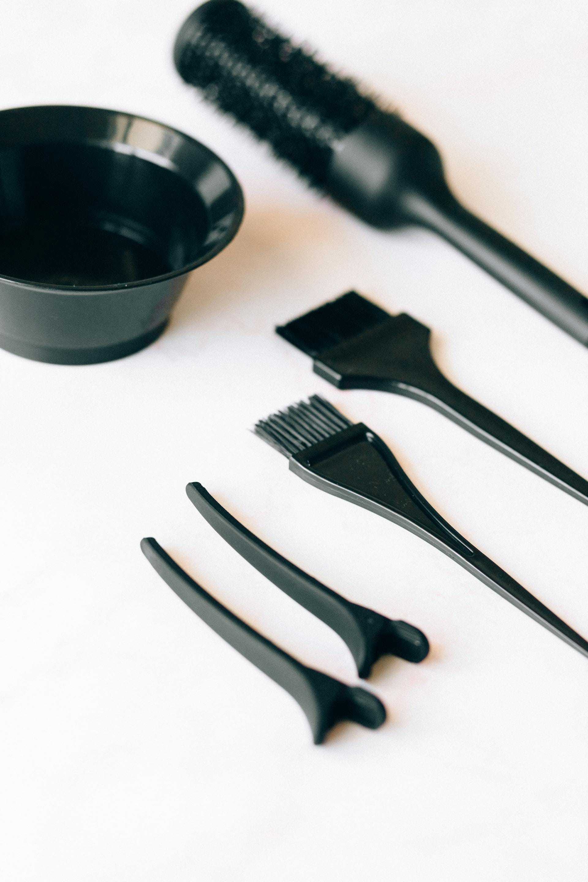 Hair coloring tools: brush, bowl, comb, and sectioning clips on a white surface.